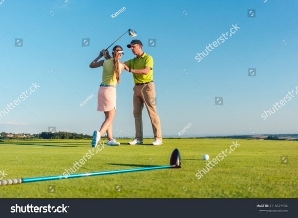 stock-photo-full-length-of-a-skilled-golf-instructor-teaching-a-young-woman-to-swing-the-driver-club-for-a-1116629534
